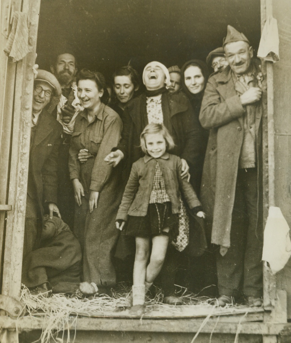 Safe At Last!, 3/11/1944. Middle East—Almost hysterical with joy as they arrive at their destination—a desert camp in the Middle East—these Yugoslav refugees laugh happily from the door of a box car. Aided in their escape from islands and towns along the Adriatic coast by underground elements of the Yugoslav guerillas, 25,000 of the refugees reached the camp safely. The group consisted mostly of women and children, accompanied by a few aged and disabled men. This is an exclusive ACME photo.;