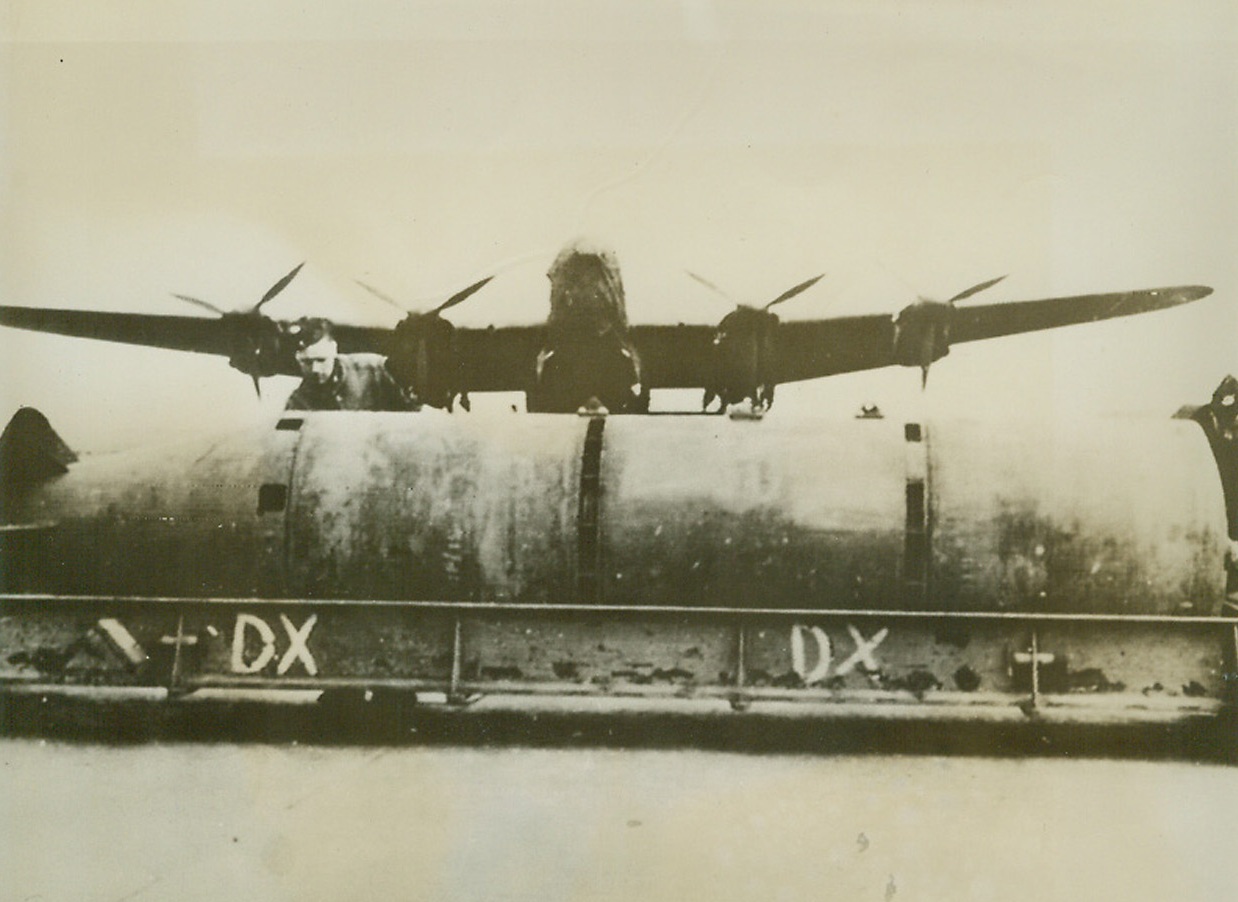 Britian’s Super Block-Buster, 3/13/1944. England—The first photo of the R.A.F.’s six-ton bomb shows the “super-super-block-buster” in front of a Lancaster bomber that carries it. The comparable size of the bomb and plane is distorted, since the six-tonner is closer to the camera than the bomber which has a 102-foot wing span. The gigantic missiles of destruction were used to blast a Nazi-directed plane engine plant at Albert, France, on the night of March 2, and a few of them leveled most of the Gnome-Rhone plane engine works in an earlier night raid.;