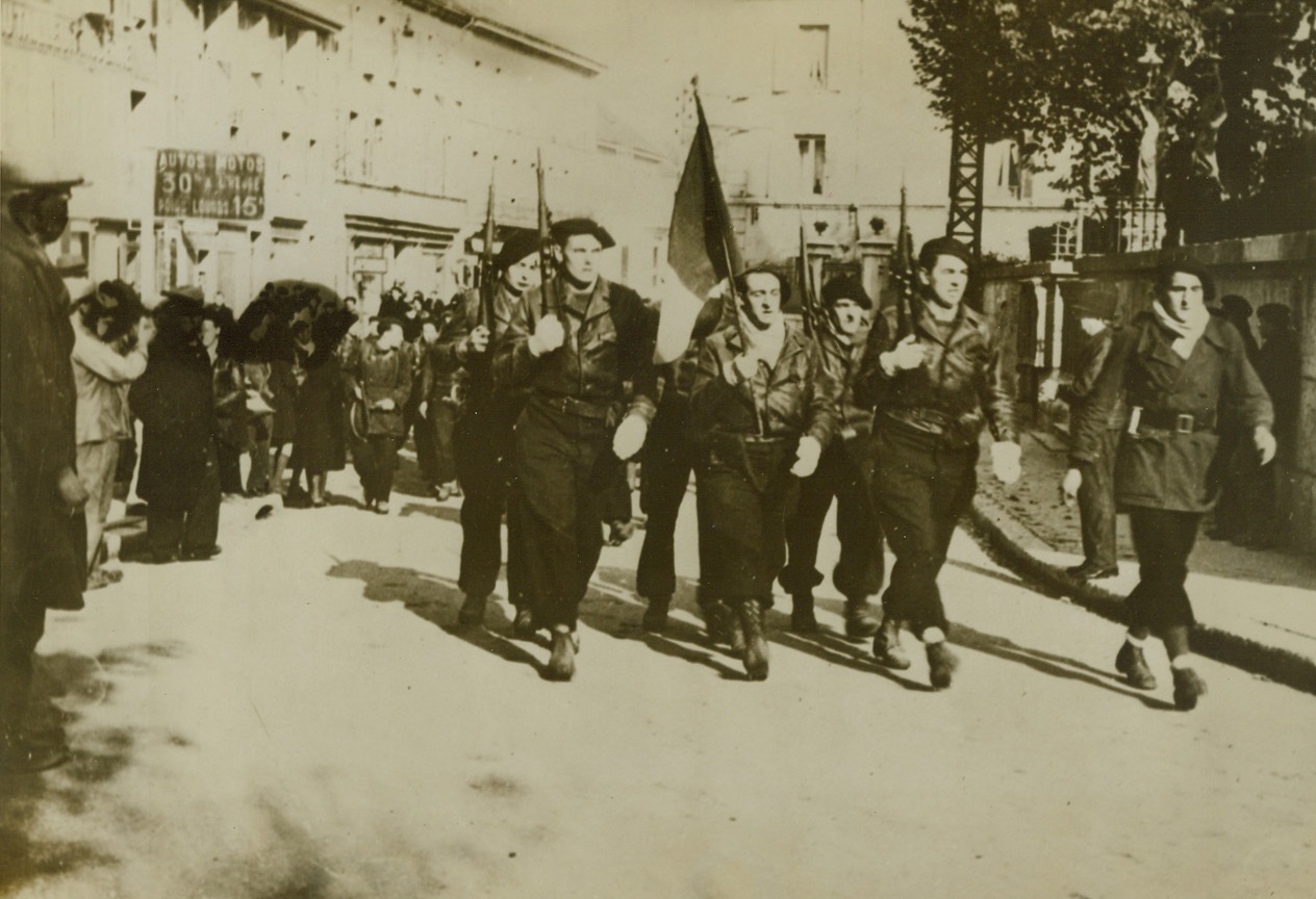 THEY “PULLED A FASTIE”, 3/28/1944. OYONNAX – Maquis warriors march through the streets of Oyonnax, 20 miles West of Geneva, on their way to an Armistice Day ceremony on Nov. 11, 1943.  Putting one over on the Nazi and Vichy authorities, who were deceived by posters announcing an Armistice Day celebration in another town, the Maquis took over the town, conducted the memorial services, sang the marsellaise, and returned to their hidden camps.  And the Nazis were waiting impatiently, 12 miles away, for the services to being.Credit: Acme;