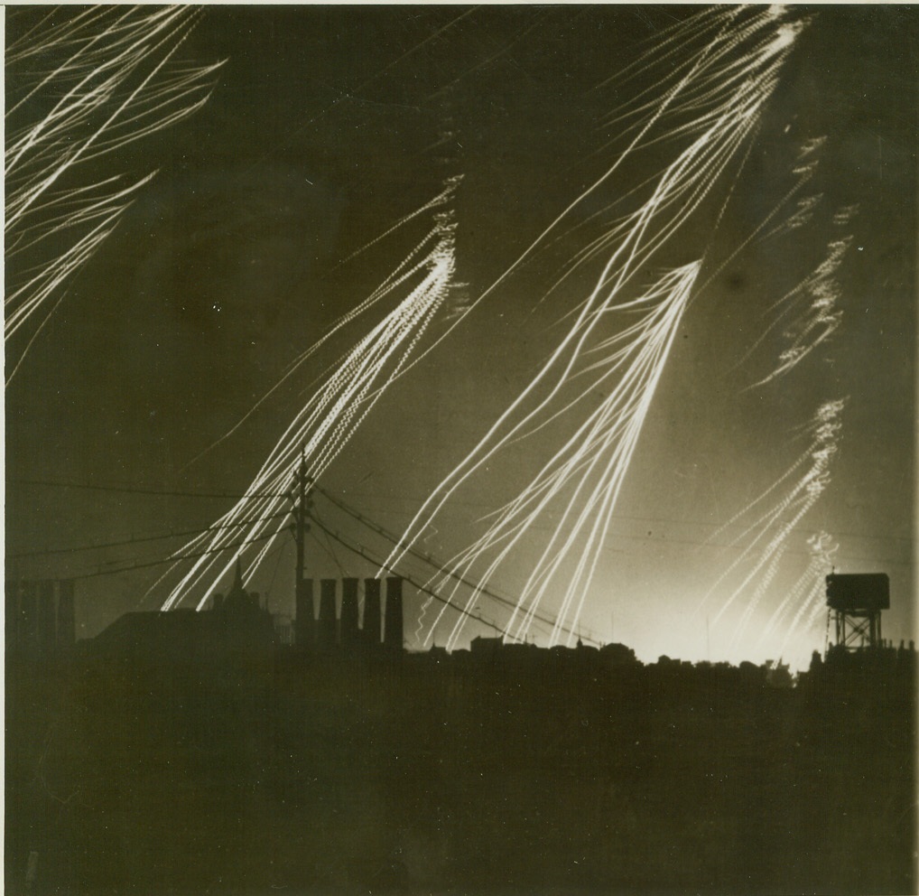 War Lightning Over London, 3/4/1944. London, Eng.—A weak Nazi raid over London is the signal for a barrage of bursting shells, pockets and new types of projectiles to be sent up by the defending British. Flares and flak make a silhouette of the rooftops and the continental roar of the anti-aircraft barrage far exceeds the sound of exploding Nazi bombs. Credit: ACME;