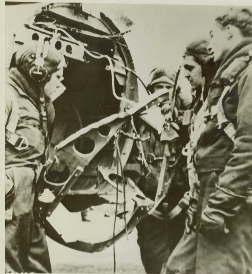 Lost Their Tail Gunner, 3/27/1944. England—The crew of an American bomber look sadly at the after end of their ship, following their return to a base in England. The tail gunner, and their buddy, was at his post when a burst of flak knocked a section of the plane’s tail off over Hamm, Germany. Left to right, are: Sgt. Ollie Crenshaw, of Birmingham, Ala.; S/Sgt William Blakeney, Little Rock, AR; Sgt. Bernard Bendin, East Chicago, Ind; and S/Sgt Seymour Berman, of New York City. Credit: U.S. Army radiotelephoto from ACME.;