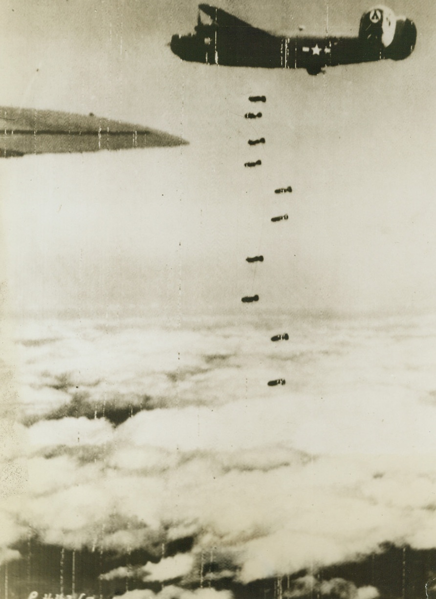 Bombs Away – Over Romania, 4/29/1944. Romania has felt the weight of our air might before. This picture was taken during a recent raid by the 15th Army Air Force on the marshalling yards at Ploesti. A B-24 Liberator is seen dropping its load of eggs on it’s target. Ten bombs may be seen descending.  Credit: Army Radio telephoto from ACME;
