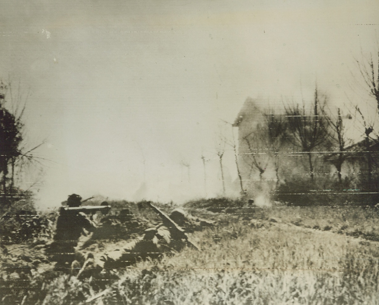 BAZOOKA “MUSIC” FOR NAZIS, 4/19/1944. ITALY—Allied Infantrymen, (left), use a bazooka to blast Germans from this farmhouse (right, background), along the Anzio front. The weapon, (on shoulder of man at far left), has just fired a shell which can be seen exploding to the left of the house.Credit: U.S. Signal Corps Radiotelephoto;