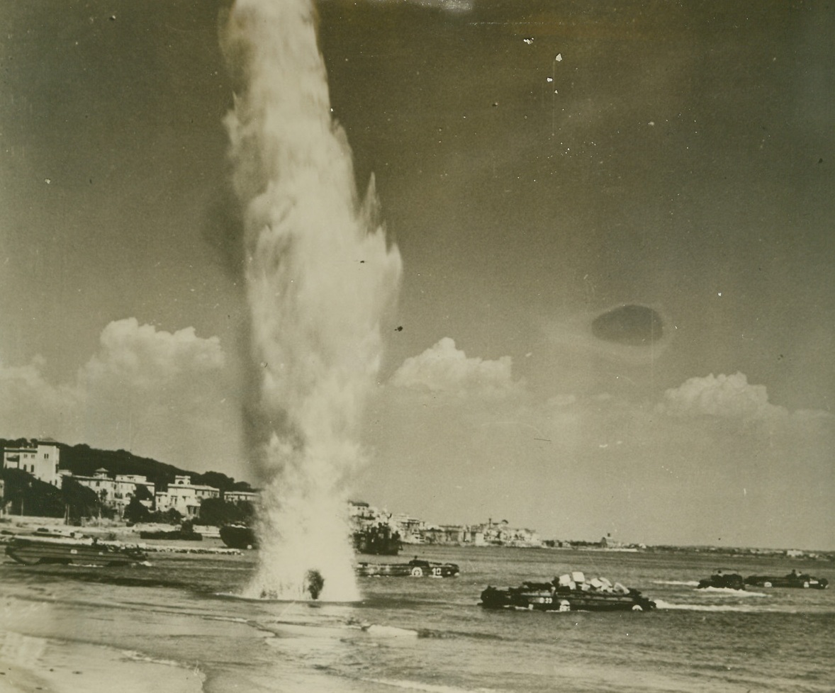Nazi "Reminder", 4/27/1944. ANZIO, ITALY -- The camera catches the explosion of a Nazi shell, which throws a column of water high into the air narrowly missing an amphibious DUCK headed for the beach at Anzio. The shell served as a reminder to Allied forces operating the beachhead supply line that they are still within range -- and within danger. The DUCK in the foreground is heavily loaded with supplies, while the others, (background), are empty and headed out to transports for a refill. Credit Line (U.S. Navy Photo from ACME);