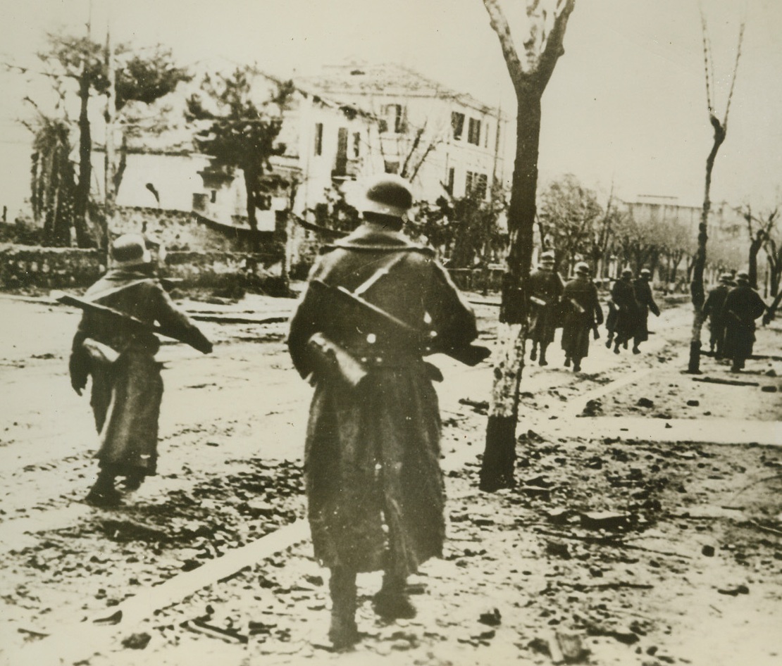 Germans Pass Through Allied Wake, 4/23/1944. ITALY – This photo which reached New York from Lisbon shows, according to the caption accompanying the picture, “German shock troops passing through the street of an Italian town in the Nettuno bridgehead area.” The rubble and ruin was caused by “a heavy Anglo-American Navy artillery bombardment March 24.”Credit Line (Acme);