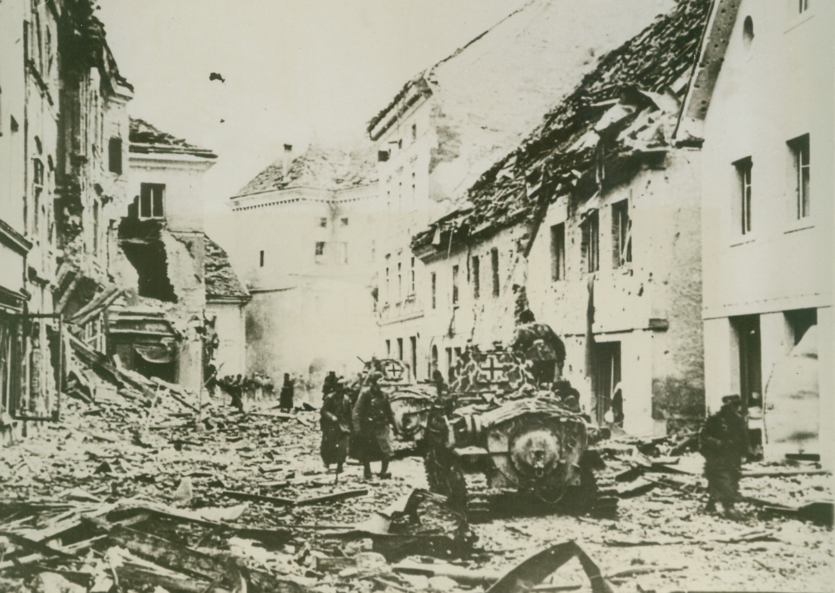 Destruction Follows German Troops, 4/23/1944. ITALY – Caption accompanying this picture received in New York from Lisbon described it as made in an “upper Italian town.” A German police unit which occupied a castle there “was attacked by a group of partisans who had taken possession of the town and besieged the German force for ten days.” A German relief unit is shown making its way through the battle-scarred streets of the partisan-held town.”Credit Line (Acme);