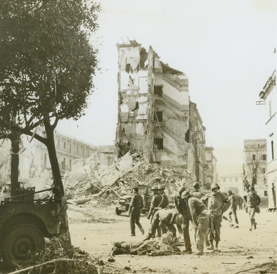Anzio in Ruins After Heavy Battle, 4/22/1944. ANZIO, ITALY – Enemy resistance met by the Yanks when they stormed Anzio was heavy, as evidenced by the ruins in this street scene. Continuous shelling made a shambles of this street, which was in perfect conditions when the troops landed. in the foreground, a wounded soldier is being placed on a stretcher. Credit (Acme) (WP);