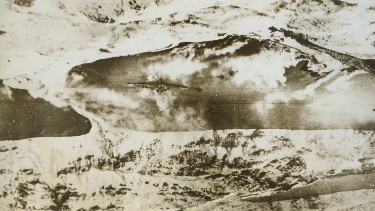 Battleship Tirpitz in Flames, 4/15/1944. Norway – Smoke screens fail to hide the German battleship Tirpitz from the waves of Baracuda Bombers that crippled the vessel hiding in Kaa Fiord, Norway. Scores of carrier-based fighters formed the escort for the bombers in their successful mission. Credit: ACME;