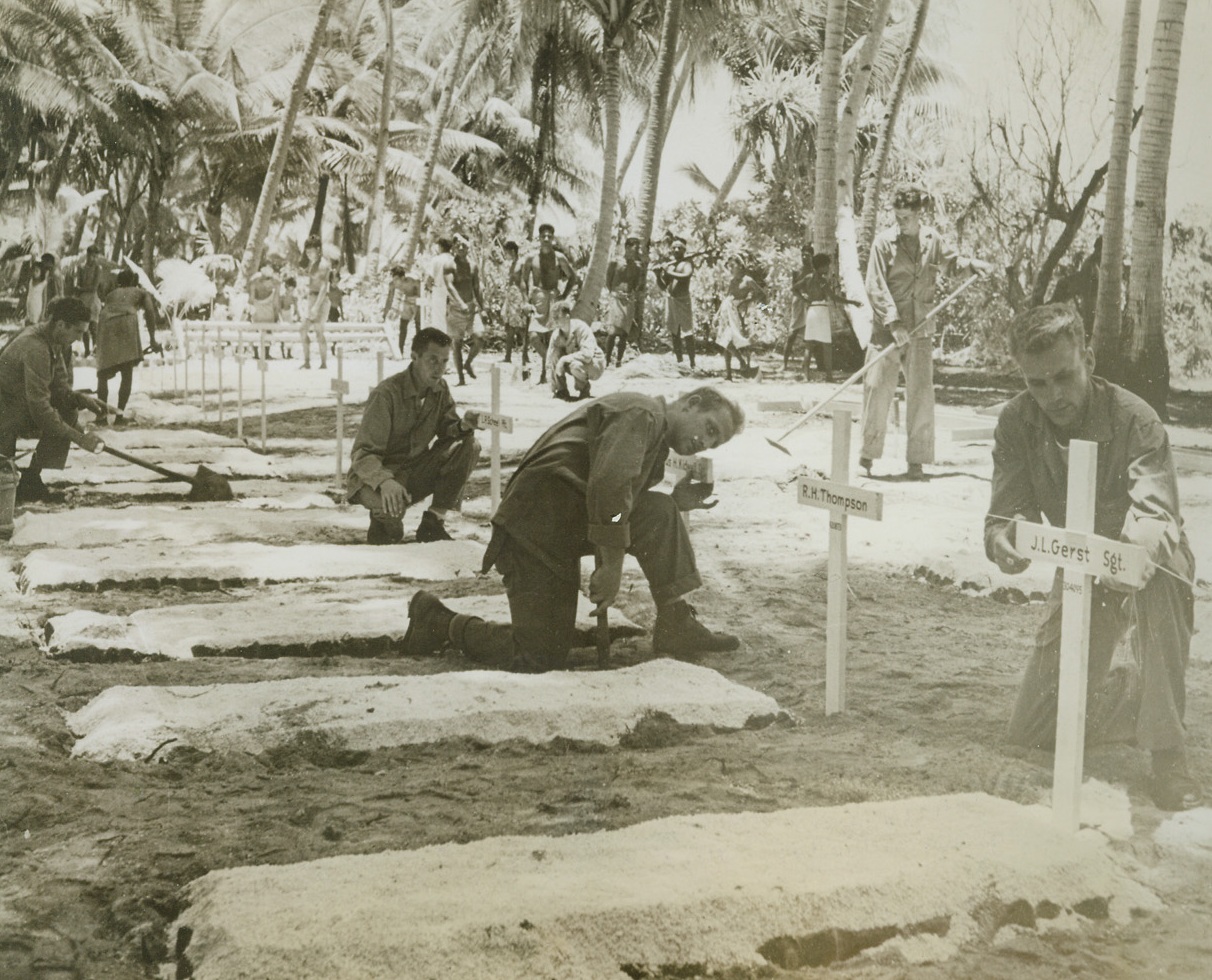 IN MEMORIUM, 4/8/1944. BURICKI ISLAND—As a final gesture toward those buddies who fell in the  last stages of the Tarawa campaign, marines tend the graves of their dead. Buried close the spot where they fell, the Leathernecks lying in this cemetery on Buricki Island were killed by a Jap Ambush just before the campaign ended. Natives had marked the graves with bottles and crude crosses, but the marines have replaced the markings with neat, white crosses. Credit: ACME.;