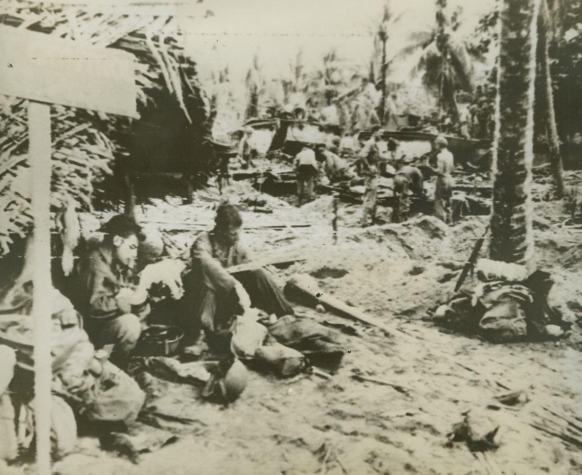 Mac Arthur’s Forces Capture Hollandia, 4/26/1944. This photo by Acme photographer Thomas L. Shafer and flashed to the U.S. by radio telephoto shows American troops resting among the wreckage of the Jap base at Korako, in the Hollandia area of New Guinea.  The smashed installations give an idea of the tremendous sea and air bombardment put down by allied craft prior to the landing. Credit line (ACME photo by Thomas L. Shafer for the War Picture Pool via Army radio telephoto);