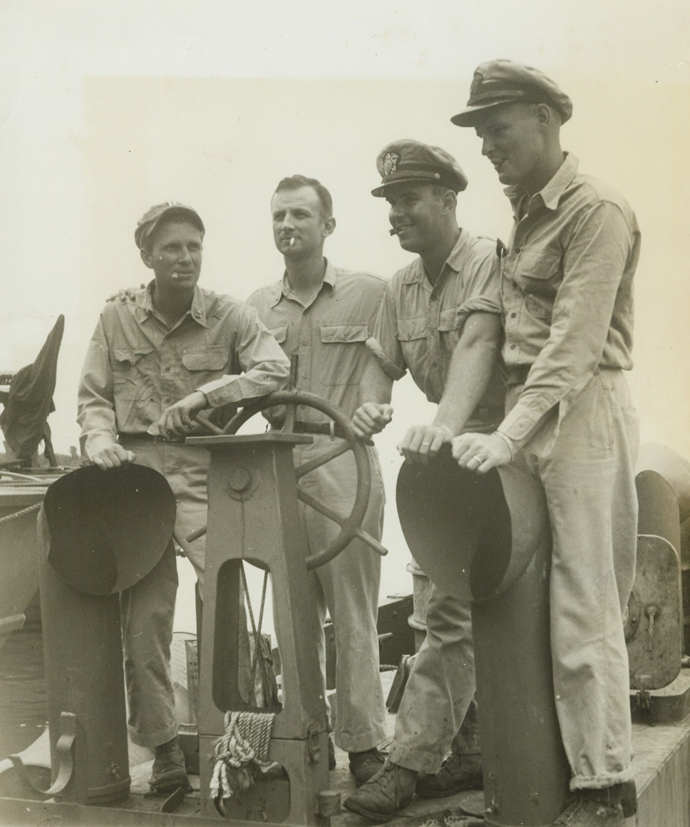 Under New Management, 4/4/1944. New Guinea – Four U.S. Navy PT boat skippers at the wheel of a captured Jap barge, which is now serving with the allies, at a base “somewhere in New Guinea.” Left to right, are: Lt. Edward P. Farley, of New York city, who commands a craft which has two enemy barges and part of a third to her credit, has sunk an enemy PT boat and destroyed two planes; Lt. Cmdr. John Harllee, Washington, D.C., who has seven barges and one enemy lugger to his credit; Engsign Robert Hunt, Marshalltown, Iowa, who is credited with fight and one-half enemy barges and one Jap “Betty” bomber; and Lt. (JG) Rumsey Ewing, of St. Louis, MO., who has a large score of seven barges, two planes, one lugger, one picket boat, one ketch, and one cargo boat.  Ewing and Farley both hold the silver star, won after their two PT boats were attacked by 30 Jap dive bombers for 45 minutes.  They shot down four of the attackers and got back to base safely. Credit line (ACME photo by Thomas L. Shafer for the War Picture Pool);