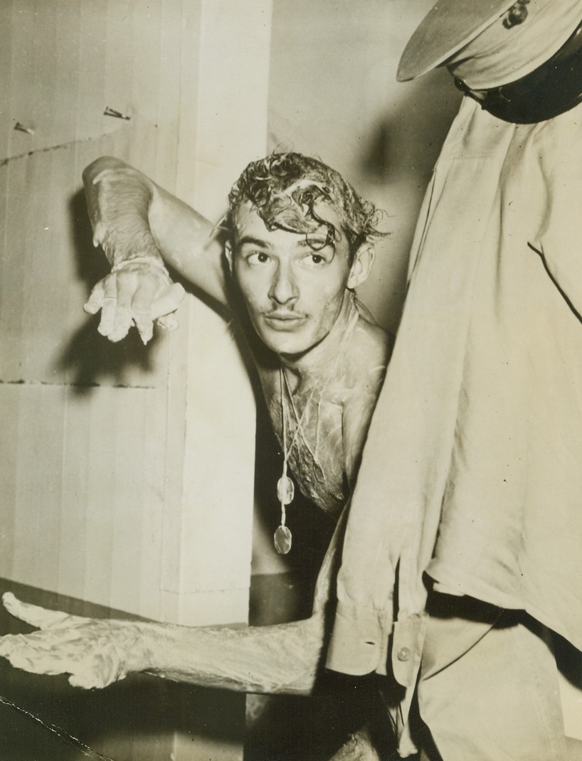 Marine Cameraman Showered the Japs, 4/22/1944. South Pacific – Taking time out from a shower to tell of his saga against the Japs, Marine Pfc. Burt B. Balaban, of Bye, N.Y., demonstrates how he dropped his rifle, gas mask and canteen on enemy installations on Wake Island during a raid on that base.  A combat photographer, Balaban was leaning out of the camera hatch taking pictures of the strike, when an enemy anti-aircraft shell exploded under the plane.  The force of the blast nearly threw the cameraman from the plane, but he pulled back just in time—to see his gear floating down toward the foe. Credit (Official U.S. Marine photo from ACME);