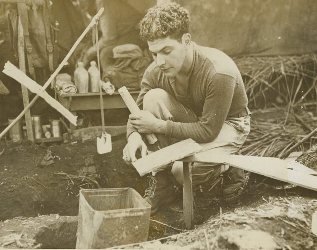 RAT TRAP FOR RATS-AND JAPS-IF THEY FIT, 4/15/1944. CAPE GLOUCESTER – Marine Sgt. Phillip J. Bianco, Cleveland, O., demonstrates his rat trap designed to rid Cape Gloucester of the furbearing animal – and the two-legged one if he can fit.  The first night it was in operation 10 rats, fur-bearing, met their doom.  A 55 gallon drum replaced the five and 65 rats were caught in one night.  The rat walks up the runway to get the food but the last section gives way under his weight and he drops into the can and to his death.Credit: Acme;