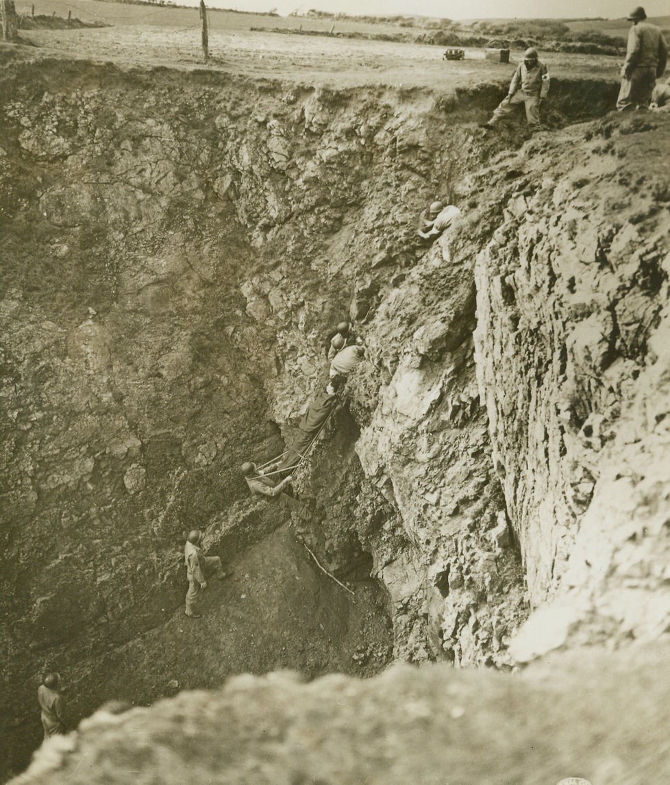 Cliff Evacuation #3, 4/28/1944. England – Combat medical soldiers of the U.S. Army are men who go into the front lines armed only with a small kit of first aid materials, administer to the wounded under fire and who return only to carry a stricken man to safety. Near a stretch of rugged coastline in Great Britain, a unit of such soldiers trains every day for the jobs it will do on the coasts and interior of Europe. Here, the ascending party runs into tough going in a narrow defile in the cliff. Two soldiers back up the rescue party in case of a slip. Credit: US Army Signal Corps photo from ACME;