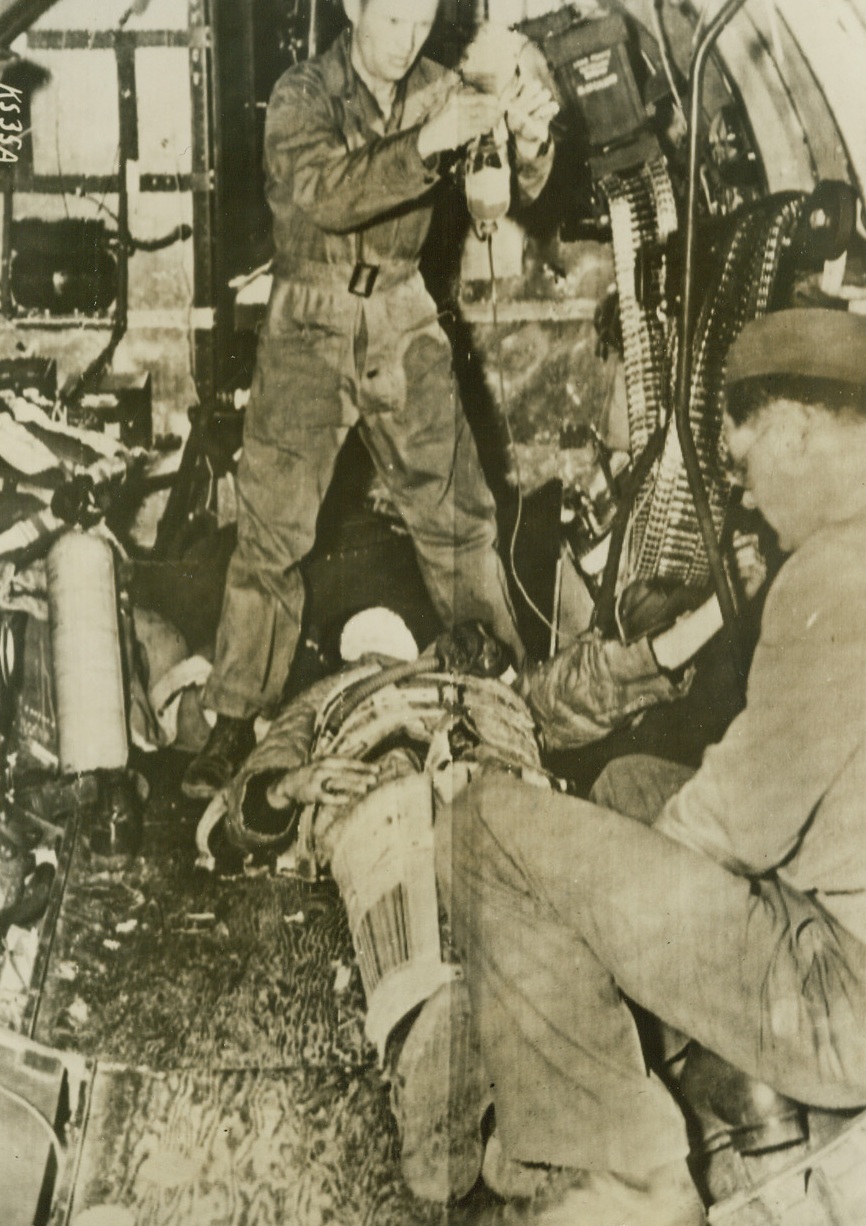 Aerial Blood Plasma, 4/3/1944. England – A wounded waist gunner gets immediate blood plasma treatment as his plane returns from attack over Northwest France. This emergency treatment was given while in the air and all medical aid will be given on the plane until the wounded man can be safely moved to a hospital. Credit: U.S. Army Radiotelephoto from ACME;