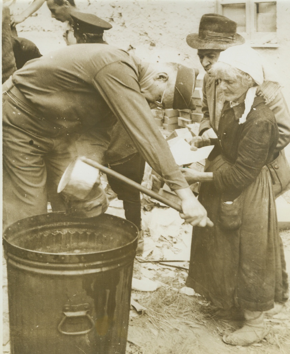 Italians Come Home, 5/31/1941. Italy – Italian civilian refugees have returned to Minturno after the Allied occupation of the town. Here an official of the Allied Military Government doles out soup for an old woman after examining her papers. Credit – WP – (ACME);
