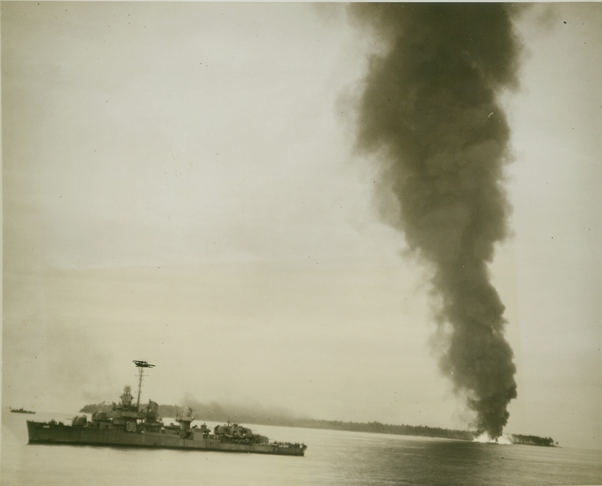 YANK DESTROYERS BLAST FUEL DUMP, 5/3/1944. DUTCH NEW GUINEA – A column of thick, black smoke towers from a blazing Jap fuel dump on Seleo Island, after a direct hit by U.S. destroyers, one of which is standing off the island at left. The island, one of three in Aitape Harbor, was attacked during the invasions of Dutch New Guinea. (Passed by censors.) Credit: ACME photo by Thomas L. Shafer for the War Picture Pool;