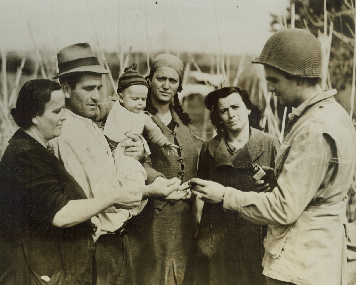 Malaria Prevention, 5/2/1944. ANZIO, ITALY—Teaching the natives the care and prevention of Malaria is one of the big chores of Allied troops in Italy. Here Pfc. Delmar Richardson of Fort Wayne, Ind., of the Medical Corps, explains the use of Atabrine in malaria prevention to a group of Italian Civilians. The natives are receiving a supply of the medicine from Richardson. Credit: ACME.;