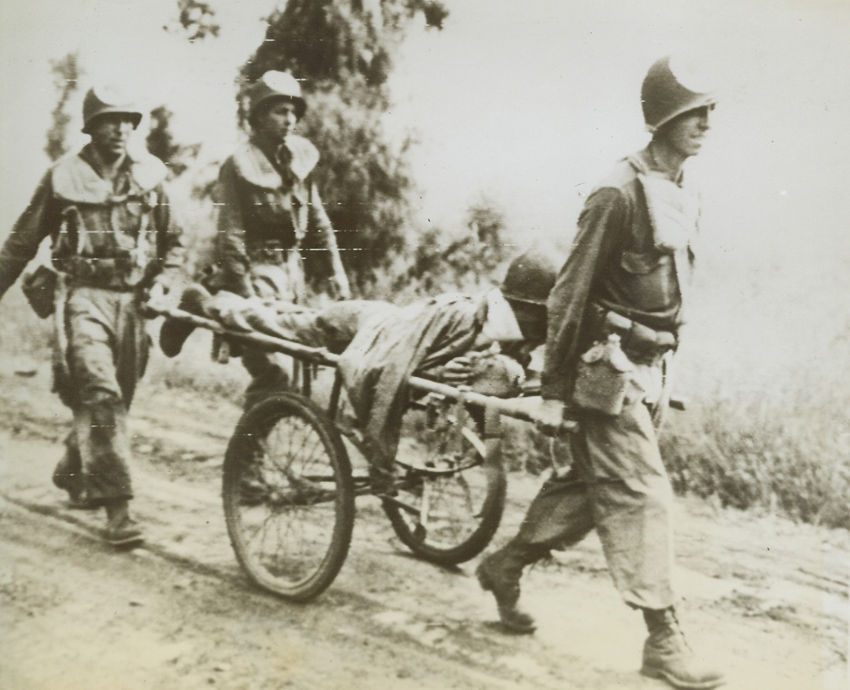 Litter-Borne Fighting Man, 5/29/1944. SOMEWHERE IN ITALY -- Returning from the Allied fighting front, this wounded soldier travels in a wheeled litter which is guided along the rough road by U.S. Army medical corpsman. The fighting man was felled at the start of the current offensive in the area. Credit: U.S. ARMY RADIOTELEPHOTO FROM ACME.;