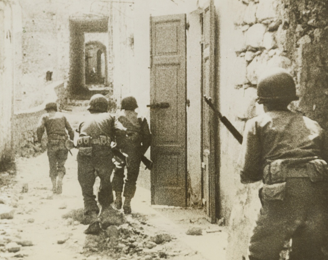 AND ONE WAS HIT (#2), 5/17/1944. ITALY—This is second photo in a dramatic sequence made in an unnamed [sic] Italian village as three U.S. scouts fought a building-to-building scrap against entrenched Nazis. Here the men try to keep their heads low as they edge cautiously toward an open door.Credit: Signal Corps newsreel photo – Acme;