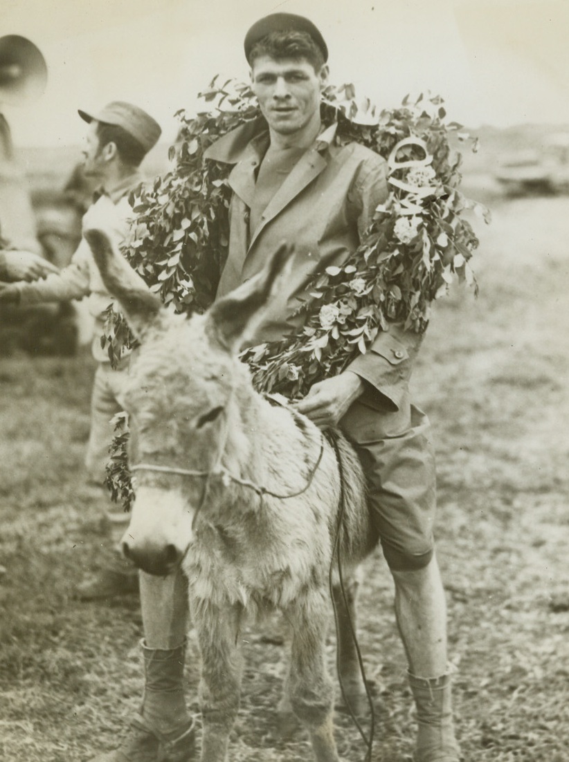 THE WINNAH—WHICH ONE?, 5/20/1944. ANZIO, ITALY—This poor little donkey certainly lives up to his other name. He did all the running in the Donkey Handicap, but stands calmly by as his rider, Pvt. Daniel L. Cason, of St. Joseph, Mo., dons the winner’s horseshoe. Pvt. Cason rode his bonny bray to victory in the handicap which was part of the rodeo staged by men of the 5th Army on the Anzio beachhead.Credit: Acme;