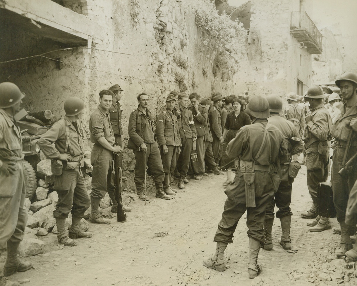 ALLIES SMASH GUSTAV LINE—FIRST PHOTOS, 5/18/1944.  CASTLEFORTE, ITALY—This photo, one of the first originals to be received in the U.S. of the current smashing Allied offensive against the Germans in Italy, shows American-equipped French troops of the Fifth Army (right, and left foreground), rounding up Germans in Castleforte after the Allies had taken the town on the second day of the attack. The enemy troops were left to hold the town “at all costs,” but were no proof against the fury of the Fifth Army attack, which cracked the Gustav Line and is now pressing strongly against the Hitler Line—last line of German fortifications in Italy. This photo, taken May 13th and which was received in the U.S. today, (May 18th) is believed to have set a new record in the expediting of news pictures by the U.S. Army.Credit: Acme photo by Charles Seawood for the War Picture Pool;