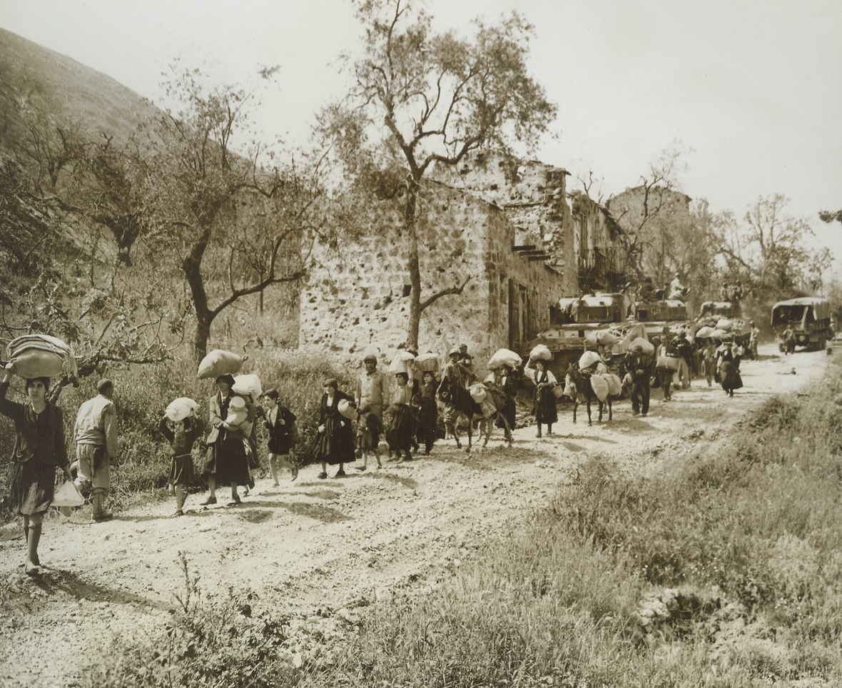 LEAVING THEIR HOMES BEHIND, 5/19/1944. CASTELFORTE, ITALY—Their possessions wrapped in tiny bundles and blanaced on their heads, Italian refugees from the battered town of Castelforte stream away from their homes, heading for safety as the battle for the town rages. Captured by French and American troops, the German stronghold fell during the second day of the new offensive in Italy.Credit: Acme photo by Charles Seawood for the War Picture Pool;