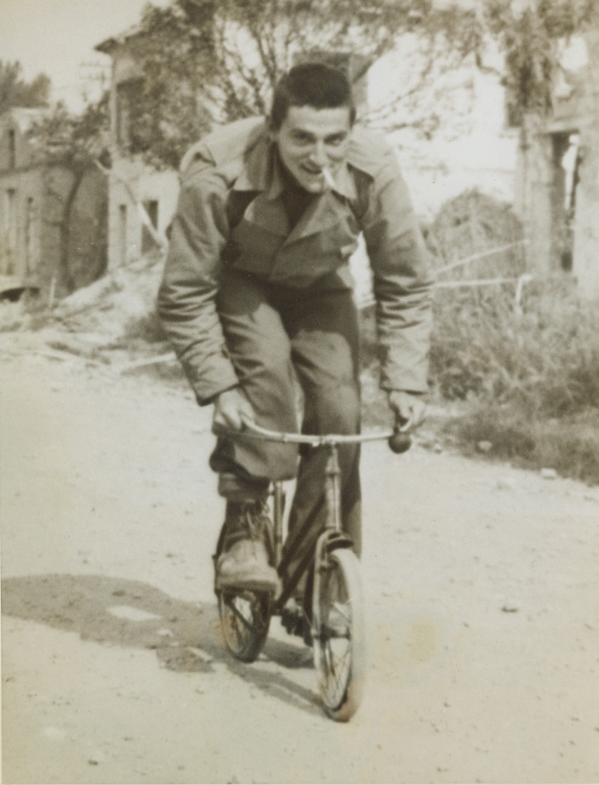 A BICYCLE BUILT—NOT FOR HIM, 5/29/1944. SCAURI, ITALY—Trundling along at snail’s pace on this diminutive two-wheeler, Cpl. Jim Ross, of Wilkinsburg, Pa., doesn’t seem at all bothered by the fact that he is joy-riding only 1,500 yards from the front lines. Cpl. Ross found the child’s bike when the American troops took Scauri in the current Allied offensive drive in Italy.Credit: Acme;