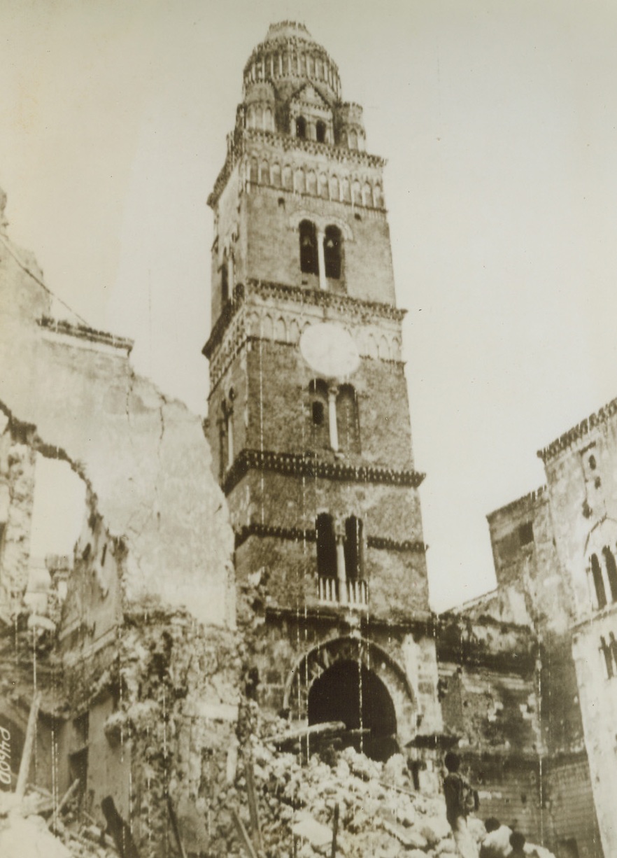 ITALIAN CHURCH ESCAPES MINE BLAST, 5/26/1944. GAETA, ITALY—Curious children stare amazed at the St. Erasmo Church, its pillar reaching high into the sky, unscathed although the buildings around it crumble to the ground after a mine blast in the vicinity of Gaeta. Main front Fifth Army troops in Italy have effected a junction with Anzio beachhead forces and are marching toward Rome from the south, while French and British forces take the northern route toward the Eternal City. Credit: US Army Radiotelephoto from Acme;