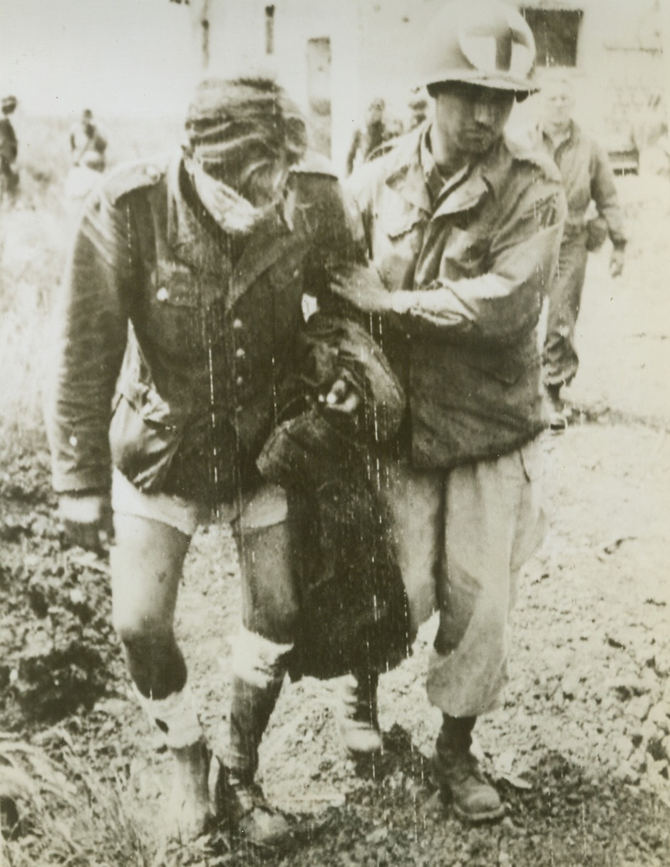 WOUNDED PRISONER GIVEN TREATMENT, 5/30/1944. CISTERNO AREA, ITALY—Wounded in both legs and the face, this German prisoner is assisted to a jeep by a US Medical Corpsman for transportation to a first aid station. The Nazi was captured by Yank forces when they took Cisterno. Allied armies are now within sight of Rome and are pounding at German defenses in the Alban Hills.;