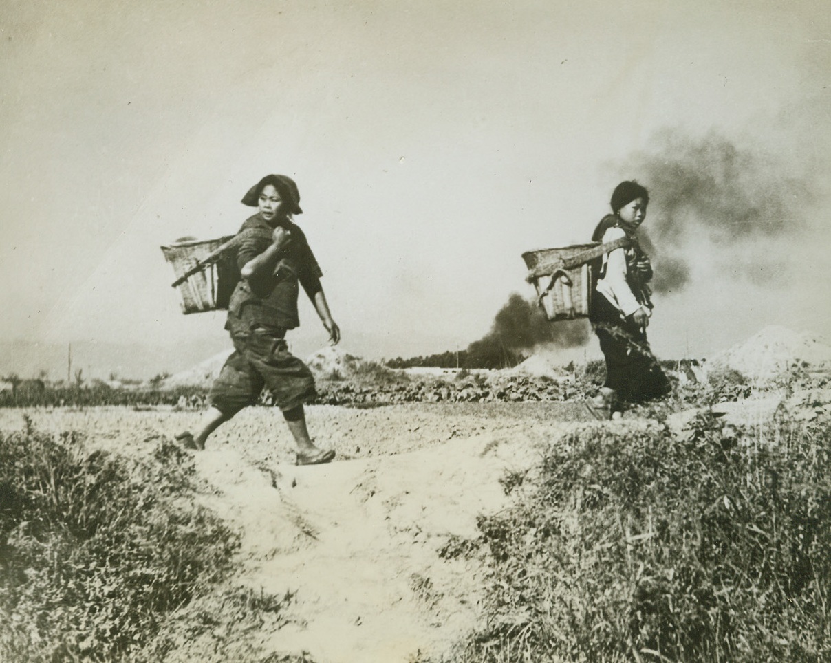 ”Jing Bow! – Jing Bow!”, 5/9/1944. Somewhere in China – As the warning cry of “Jing Bow” echoes through the area, the Chinese peasants hurriedly leave the field on which they have been working, running to the nearest shelter.Chinese for “air raid,” the cry is one that every Chinese has learned to obey at a moment’s notice. P-40 Fighters were rushing to meet the attacking enemy planes as the warning was given, and a plane, already downed, sends up a black pall of smoke as it burns in the background. Credit: U.S. Army official photo from ACME;