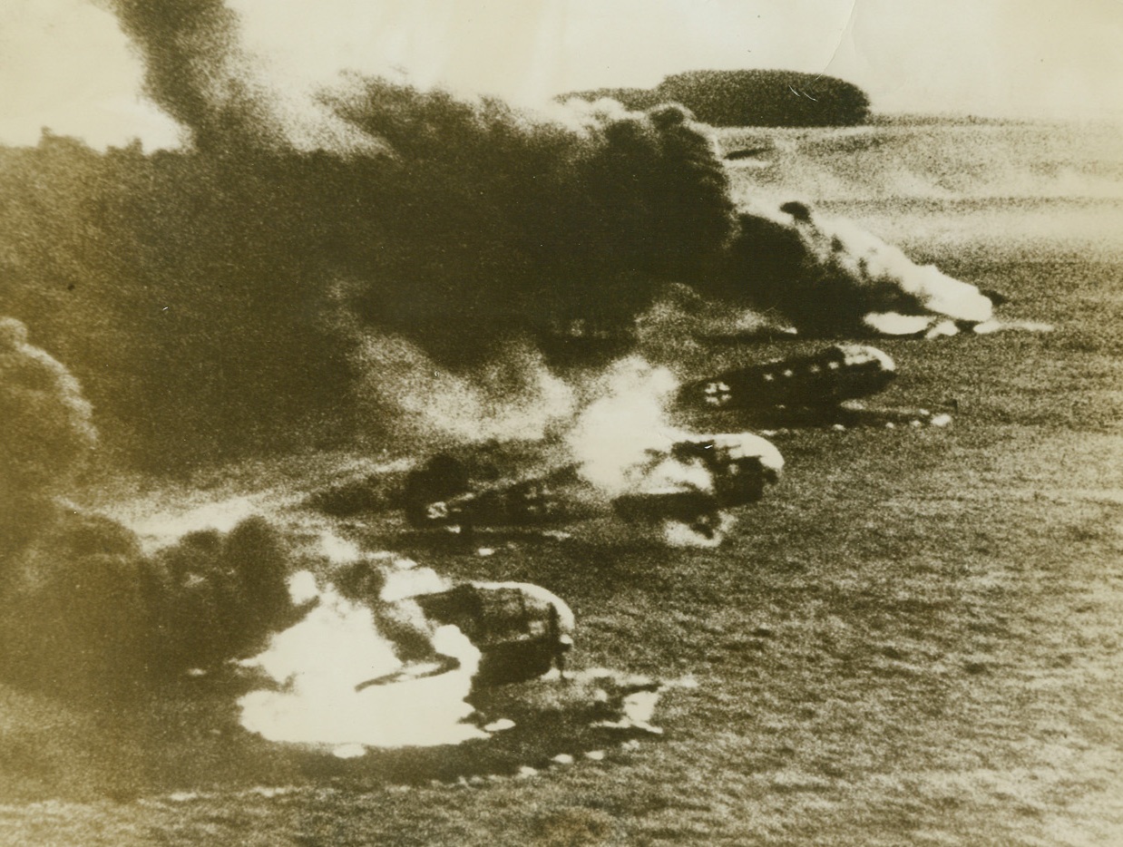 GROUNDED FOR GOOD, 5/23/1944. FRANCE – Burning furiously after an allied strafing attack, these German transports on an airdrome in occupied France are lost forever to the Luftwaffe.  During recent allied air attacks, the Nazis have been keeping a large percentage of their planes on the ground – doubtlessly conserving them for the coming invasion.  But our fighter planes zoom low, and with expert strafing, make short work of the German ships. Credit: Acme;