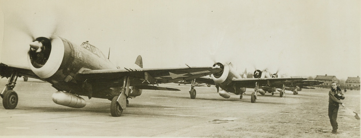 FLAGGING MEN OFF, 5/7/1944. SOMEWHERE IN ENGLAND – Lt. H.W. Collins, Army Air Forces pilot from Atlanta, GA., flags off a group of thunderbolt dive bombers as they set out on  a mission over Louvain, Belgium.  Pilots at the station take turns flagging the planes off as they roar out to smash airfields, cut communications and knock out Nazi batteries in preparation for the coming invasion of Western Europe.Credit: Acme;