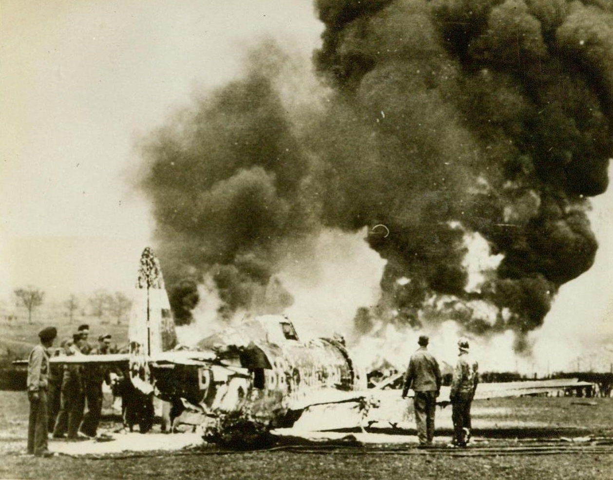Grounded By An Oil Dump - 1, 5/19/1944. Britain - Smoke rises high in the sky from the sheets of flame enveloping this Thunderbolt Fighter Plane at a 9th Air Force Fighter Base. The plane, piloted by Capt. Thurman F. Morrison, of Memphis, Tenn., was taking off when it smashed into a 40,000-gallon oil dump and immediately burst into flames. Two alert members of an Ack-Ack Unit, Pvt. Harold Smith, Framingham, Mass., and Dominick J. Camonarano, Bronx, N.Y., perceived the plight of the trapped pilot, hacked the canopy from the cockpit, and rescued Capt. Morrison. Credit: USAAF photo from ACME;