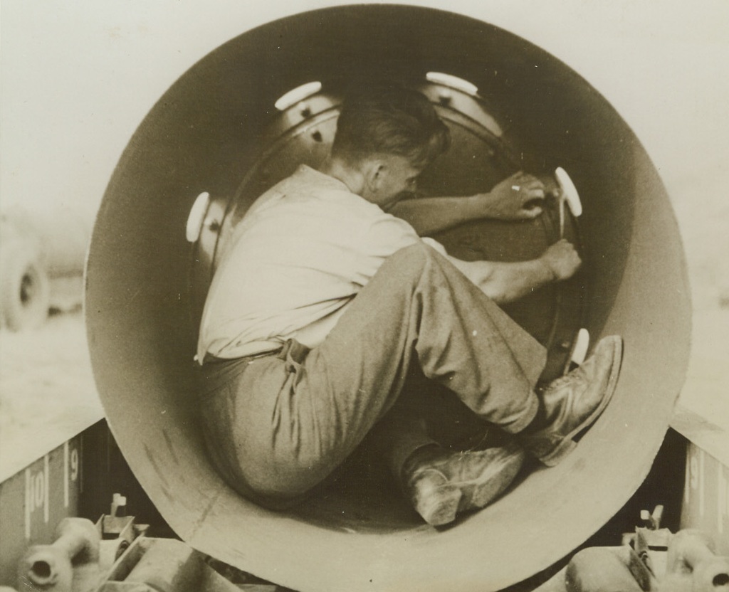 He’s Playing with Dynamite!, 5/8/1944.England – This armourer is working in close and dangerous quarters as he makes adjustments inside the fin of an 8,000-pound bomb. Night after night, these famous “blockbusters” of the RAF bomber command screech earthward from RAF bombers over enemy territory. German industrial and transportation centers have been almost impossibly crippled by these devastating raids. Daylight follow-ups by the AAF smash at vital enemy points. Credit: ACME;