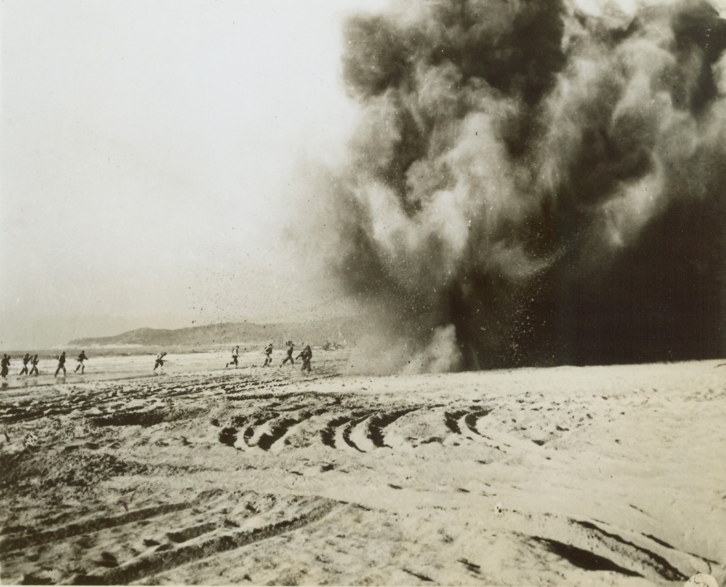 Practice Makes Perfect, 5/5/1944. England – Dodging shell bursts as they rush across the sandy beach, these American infantrymen go through some rugged training for the coming invasion of the continent. Working under realistic conditions, amphibious forces land on the beach and storm “enemy” beach defenses amid explosive charges which simulate enemy artillery bursts and bombing. Working on the theory that “practice makes perfect,” amphibious maneuvers of this type are being conducted throughout England. Credit: Official US Army photo from ACME;