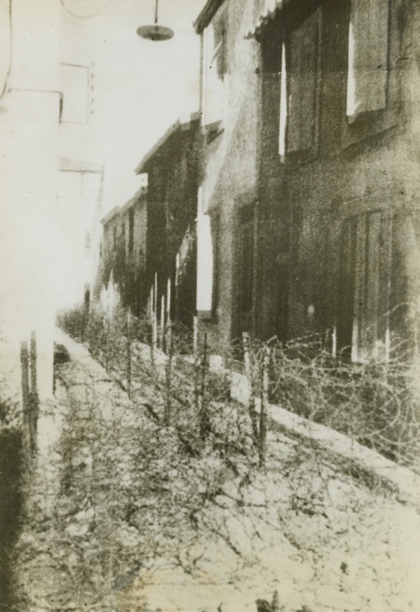 German Invasion Defense, 5/22/1944. France – Streets leading through a French fishing village from the beach are mined against tanks and filled with barbed wire obstacles to impede assault troops. This picture, received from London through a neutral source, shows one method the Nazis have adopted to attempt to obstruct the Allied forces making the sea-borne invasion of Europe. Credit: ACME;