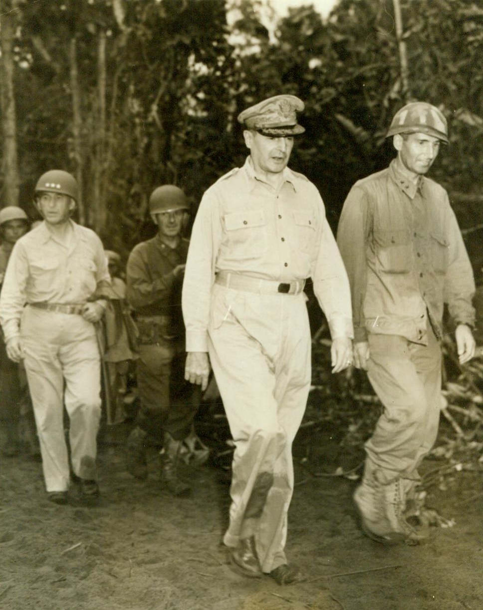 MacArthur Makes an Inspection, 5/8/1944. New Guinea—Gen. Douglas MacArthur (Center) makes a preliminary inspection of the newly captured bay area, in Hollandia. With the Allied Chief are Lt. Gen. Walter Kruger (Left) and Maj. Gen. Fred Irving (Right). Yank Soldiers eager to get a “look-see” at the land they invaded follow their General into the densely wooded area. Allied forces invading important Jap strongholds in Dutch New Guinea recently took the enemy by surprise and met very little resistance, and succeeded in capturing the important Japanese airfield at Hollandia, a strategic move in the battle for control of the Pacific. 5/8/44;