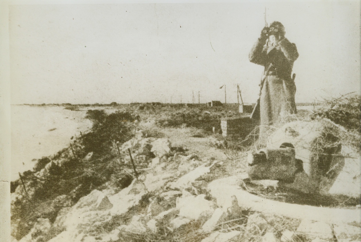 On the Look-Out for Invasion Forces, 5/22/1944. FRANCE-- A German sentry in a French fishing village looks out to sea--on the look-out for any sign of Allied invasion troops. Stretching along the coast are small concrete gun emplacements like the one in the foreground. Barbed wire entanglements line the beach. Nazis have been thorough in setting up invasion defenses to impede our forces when they make the seaborne assault against the Atlantic Wall. Credit: (ACME);