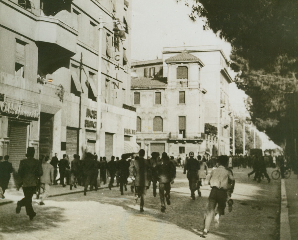 Lone Fascist Wages Own War, 6/24/1944. ROME, ITALY—When American Forces entered Rome; they were greeted by an unseen enemy. One lone fascist sniper opened fire on the soldiers from the window of an apartment house, but he was quickly nabbed by the Yanks. Here, a crowd of Italian civilians scurry for shelter from the sniper’s fire.  Credit: Canadian Official Photo from ACME.;