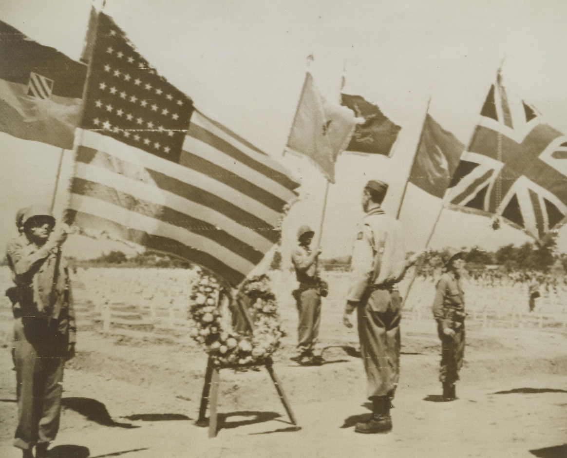 Italian War Dead Honored, 6/1/1944. ITALY—Flanked by Allied flags, Lt. Gen. Mark W. Clark stands at attention before an easel on which he placed a memorial wreath honoring the Allied fighters who died fighting in Italy. General Clark pledged “To those men who lie before us that the Fifth Army shall continue to fight where they left off, with their spirit as our guide, till victory is ours.” Credit: U.S. ARMY Radiotelephoto from ACME.;