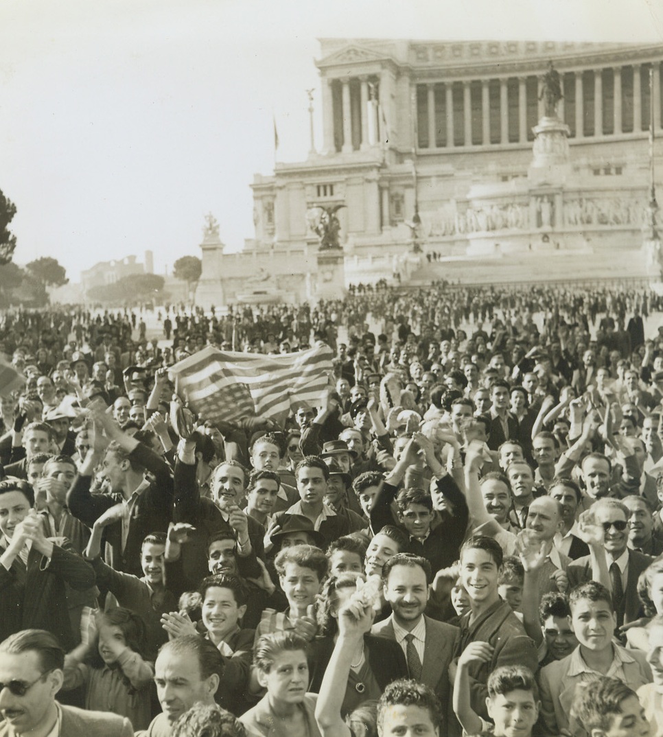 Hallelujah Day, 6/10/1944. ROME, ITALY—With the entrance of the conquering American troops into their city, Italian civilians realized that the day of Rome’s liberation was at hand. Filling the air with their cheers and cries of joy, they massed in the streets to pay honor to the Yanks. Here a crowd in front of the Victor Emmanuel Monument lifts aloft the stars and stripes as they hail the conquering heroes. Credit: ACME photo by Charles Seawood, War Pool Correspondent;