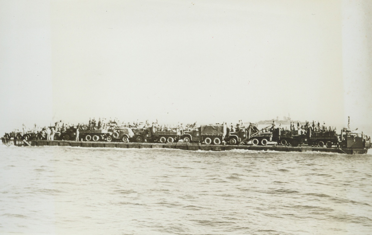 “RHINO FERRY” FOR INVASION FORCES, 6/6/1944. The most difficult phase of the initial operation against the European Continent—that of bridging the last few hundred yards between vessels and the beach—is being accomplished to a large degree through the use of the U.S. Navy’s modern pontoon gear. Made up of hollow boxes of welded metal, in two sizes, a huge, self-propelled barge, called the “rhino ferry” can be put together aboard ship. When the objective is reached, sections of the raft can be lowered over the side, fastened into the whole with bolt, nuts, links, and angles. The, the “ferry” is ready to float vehicles and supplies ashore. The new style pontoons—or tanks—are built in two sizes, five by seven by five feet deep, and the other, seven by seven by five with one edge curved to serve as the prow of a barge. These rafts as a whole—or in sections—can be filled with water and used as piers or docks. Designed by Capt. John N. Laycock, Civil Engineer Corps, USN, Washing, D.C., these pontoons have been used previously in invasions of Attu, Africa, Sicily, and Italy. I this series of photos, the “rhino ferry” is shown being assembled and put to use.  NEW YORK BUREAU Loaded with motor vehicles, the “rhino ferry” heads for the beach from a transport. Credit: U.S. Navy photo from Acm;