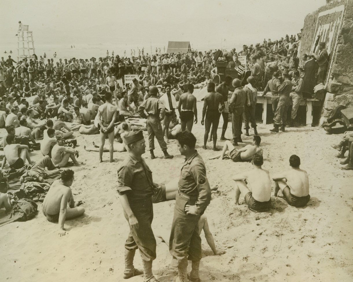 Coney Island in Italy, 6/16/1944. ITALY – In a scene similar to the one enacted with regularity at Coney Island, Yank troops of the Fifth Army get a touch of home as they lounge on a beach in Italy. A swing band plays for the boys on request and no regulations are placed on swimsuit style. Some come dressed G.I. and others in the oldest of bathing wear. New Yorkers, working in the their offices during the hottest days of the year, can look with envy at this beach scene. As a reminder that the war is still close at hand, note the screening smoke in the background.Credit Line (Signal Corps Photo from Acme);