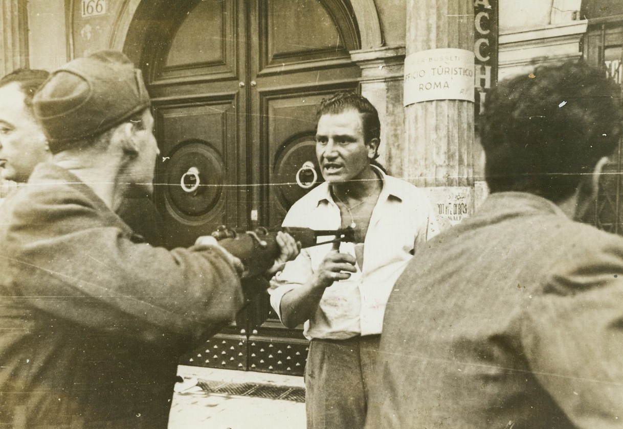 ANTI-FASCISTS HAVE THEIR DAY, 6/17/1944. ROME, ITALY—With the Allied entry of Rome, groups of rabid anti-fascists, who had long been forced underground, sprang from their hiding places, banded together and smoked out known fascists to bring them to trial and make them pay the inevitable price all fascists must pay for their lordly ways, their rule with an iron hand, and the suffering they forced upon the people. Not all reach a courtroom. The fiery Italian people have made their own rules governing the treatment of fascists. This series of pictures taken in Rome tell the story of one anti-fascist organization and the capture of some of Musso’s stooges. New York Bureau Captured in a tobacco shop along with two of his partners, this known fascist feebly tries to push aside the barrel of a rifle pointed threateningly at his chest by an Italian patriot. Groups of anti-fascists prowl through the streets of Rome now that the Allies occupy the city and mete out their own idea of a proper punishment to any fascist they can smoke out. Some are taken to trial where their fate is decided. Some never reach a courtroom. The anti-fascists in Italy can now pay back in full measure for the years they suffered under fascistic rule.  Credit-WP-(ACME);