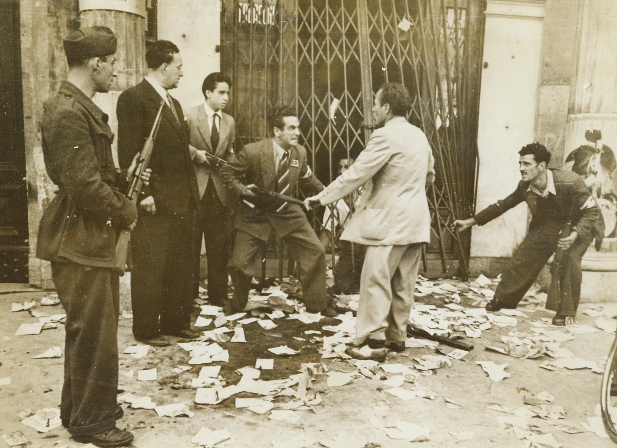 ANTI-FASCISTS HAVE THEIR DAY, 6/17/1944. ROME, ITALY—With the Allied entry of Rome, groups of rabid anti-fascists, who had long been forced underground, sprang from their hiding places, banded together and smoked out known fascists to bring them to trial and make them pay the inevitable price all fascists must pay for their lordly ways, their rule with an iron hand, and the suffering they forced upon the people. Not all reach a courtroom. The fiery Italian people have made their own rules governing the treatment of fascists. This series of pictures taken in Rome tell the story of one anti-fascist organization and the capture of some of Musso’s stooges. New York Bureau With the information that three known fascists were hidden in a tobacco shop, armed Romans blew out the front of the shop and dragged out the three men. One rabid member of the patriotic group vents his hatred in words that need no telling as a captured fascist cringes before him. Note the arm bands and lapel tags used by the anti-fascists. Another of the fascists kneels behind the grill waiting to be brought out.;