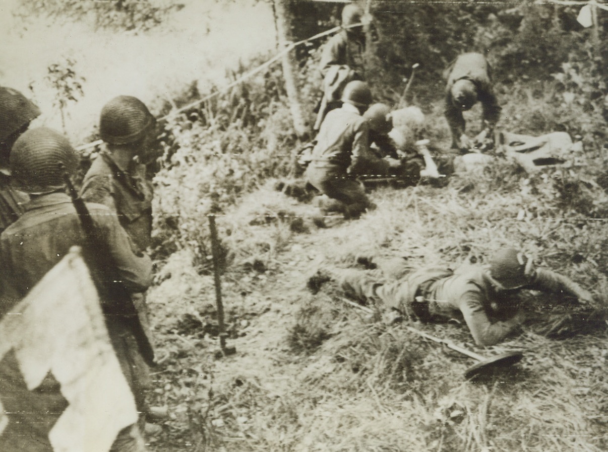CASUALTY ON THE MINEFIELD, 6/12/1944. While American medics give first aid to an American combat engineer who stepped on a German mine, another engineer searches for further mines. Before evacuating the beachhead area, the Nazis planted the surrounding fields with mines, but Allies cleared a path to make way for their advancing forces. Credit (ACME Photo by Bert Brandt, War Pool Correspondent, via US Army Radiotelephoto);