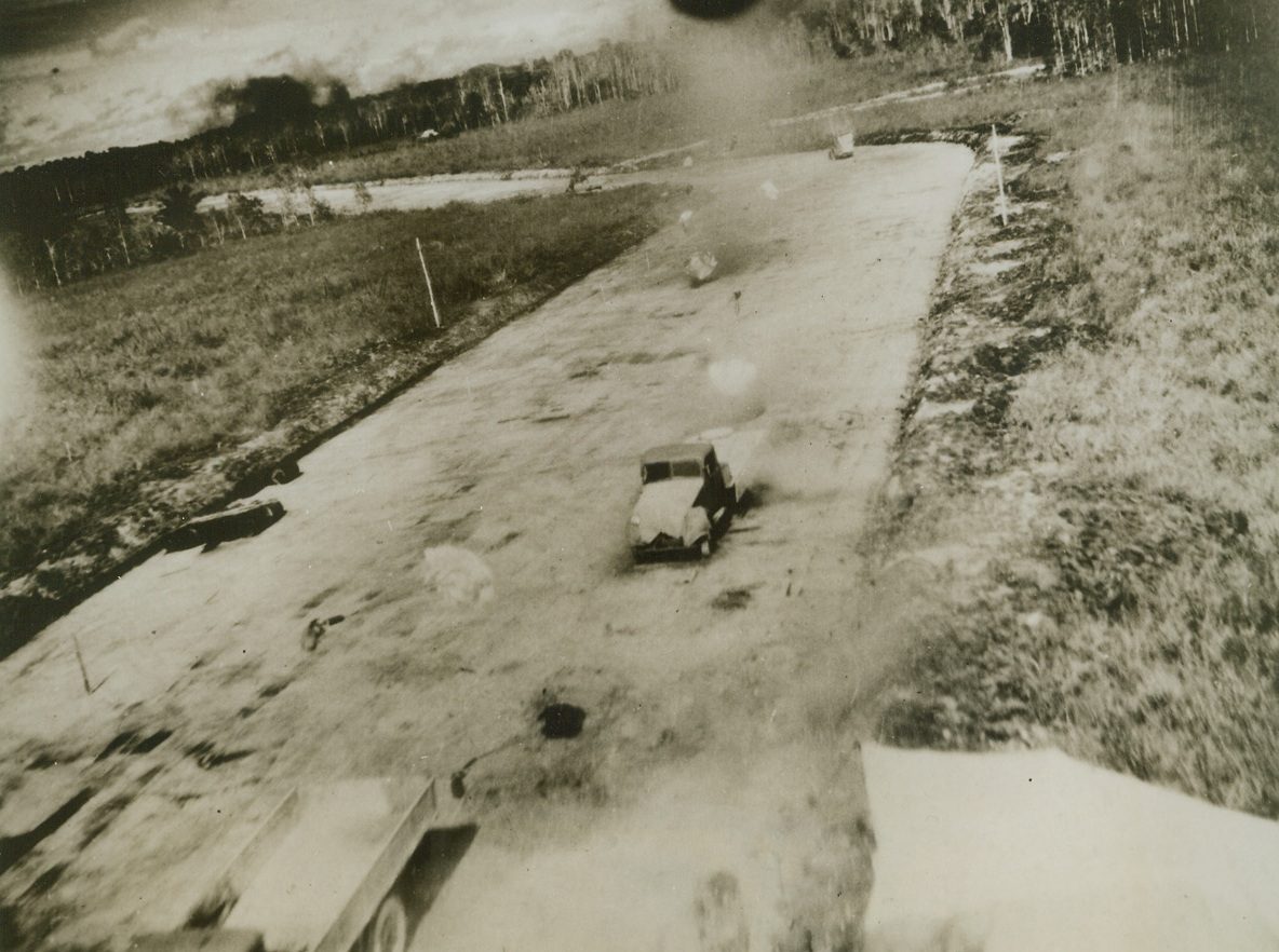 Gently Moving Death, 6/13/1944. Otawiri, Dutch New Guinea – These parachute bombs, gifts from Gen. Kenney’s Fifth Air Force Bombers, settle gently on a taxiing strip amid the abandoned trucks on the runway. Japs fled to the jungles when the bombers began the attack on the Airdrome, leaving vehicles, aircraft, and equipment to be destroyed by the “handkerchief” bombs. Credit: USAAF photo from ACME;