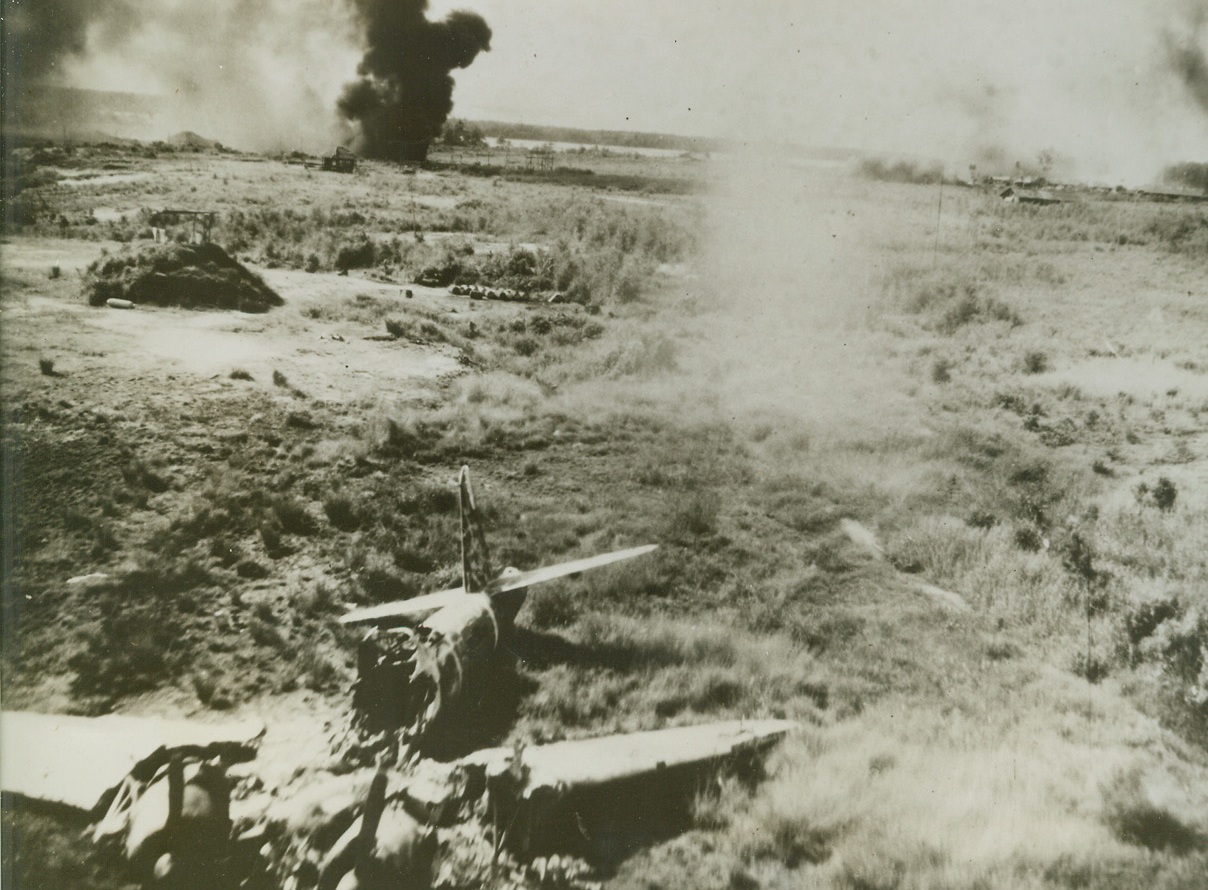 Blast Jap Airfield, 6/12/1944. New Guinea – Wrecked planes, smoke and fire are vivid proof of the effectiveness of General Kenney’s Air Force as they swoop low over a Jap Airdrome. Jap base is located at Babo, Durch New Guinea. (Passed by Military Censor.) Credit: USAAF photo from ACME;