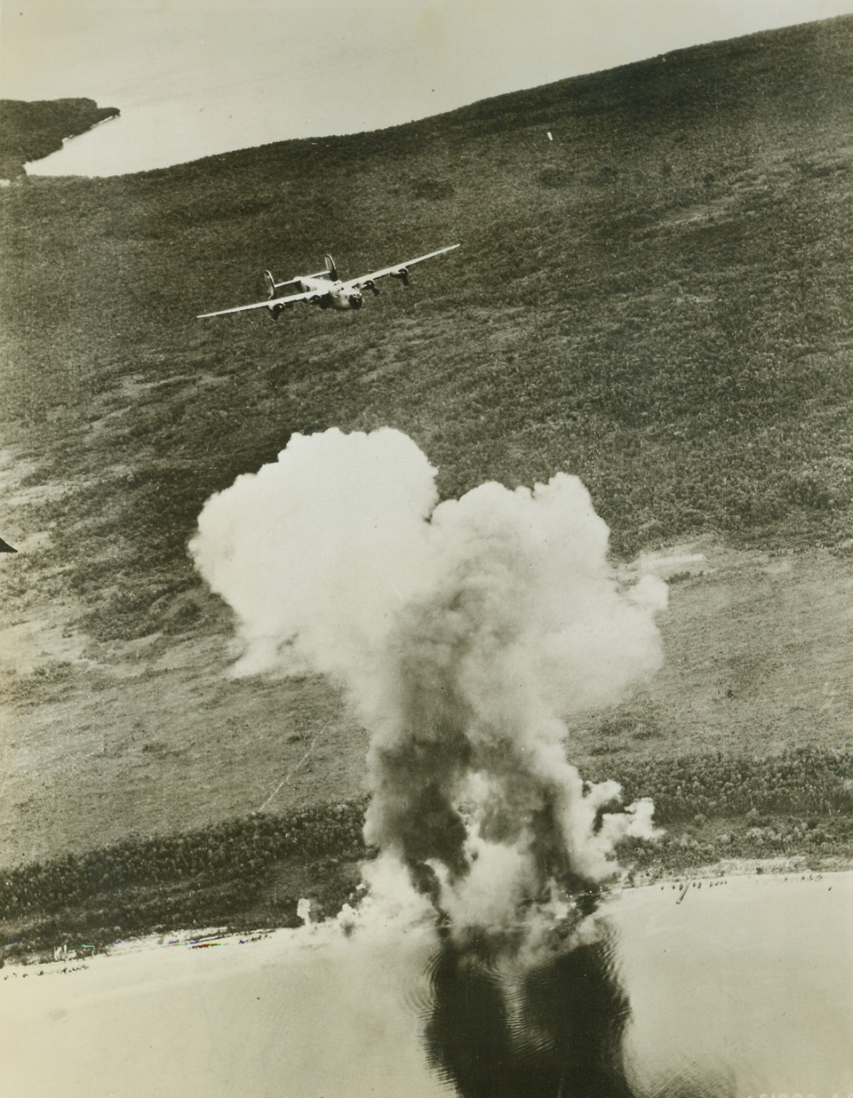 Bullseye on Jap Supply Dump, 6/29/1944. A Jap supply and personnel area goes up in a column of smoke on Biak Island, as Liberator Bombers of the U.S. 13th Air Force lay down a pattern of bombs on the narrow beach that is the target. Dark column of smoke causing the deep shadow on calm sea indicates hits on a fuel dump. Credit: USAAF photo from ACME;